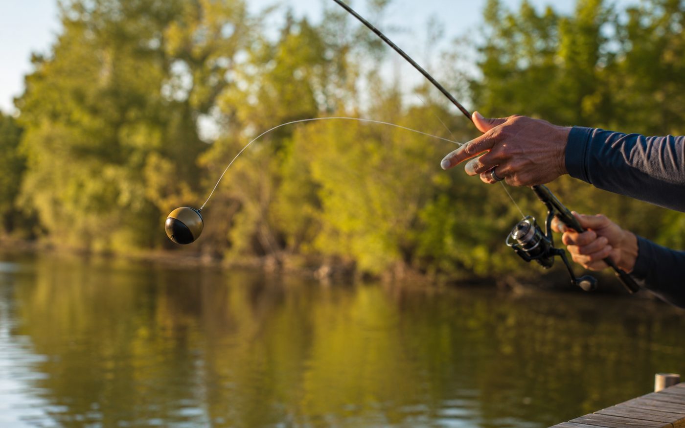 Close-up of an angler casting a small spherical castable sonar fish finder from a dock
